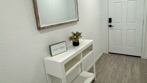 Un pasillo con una consola blanca, un espejo enmarcado y una puerta.
