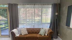 A brown sofa with patterned cushions, a large window with curtains, and a patterned rug.