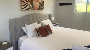 A bedroom with a tufted headboard, white bedding, and a floral artwork above the bed.