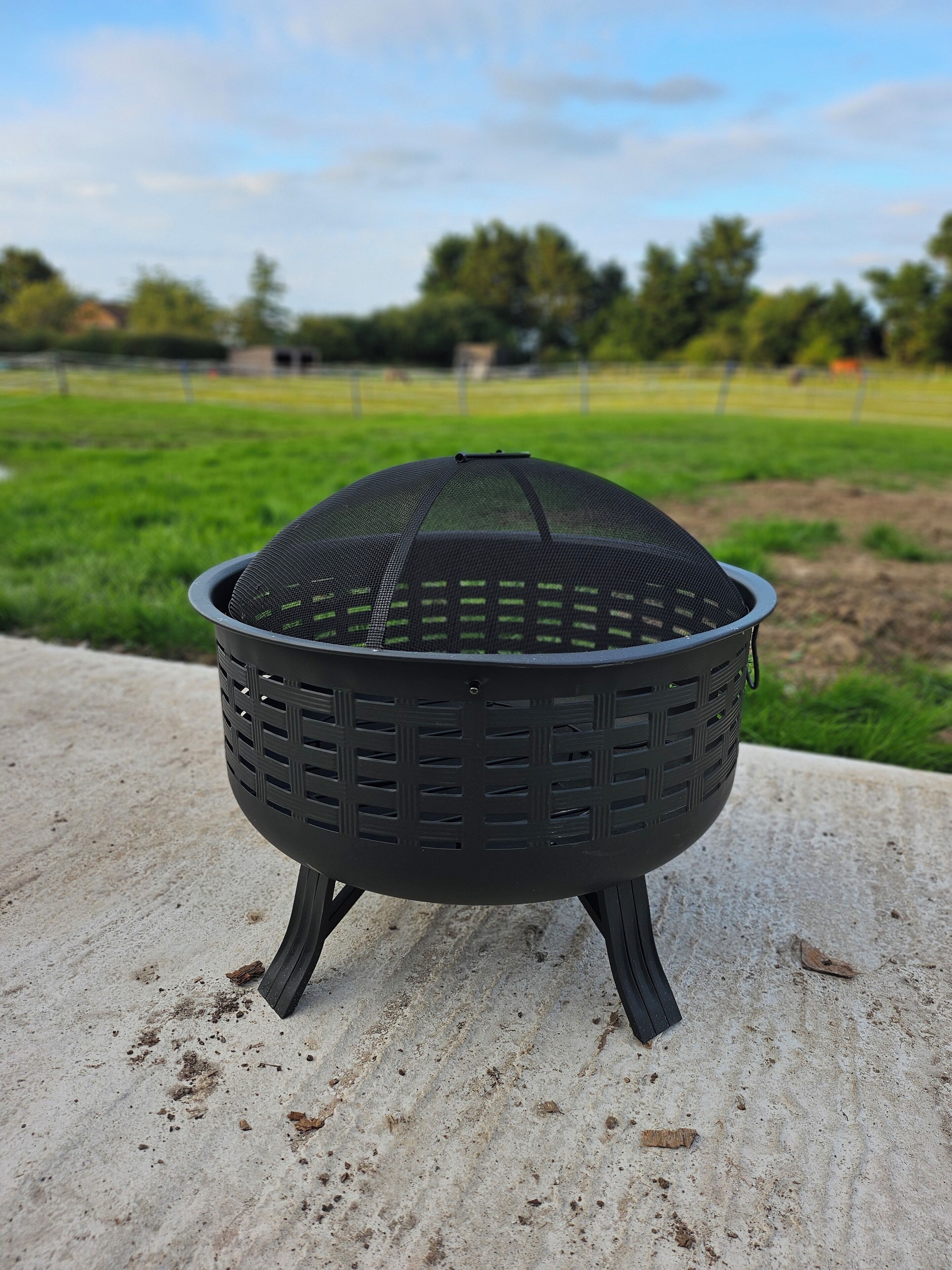 A black outdoor grill with a mesh top, standing on a concrete surface.