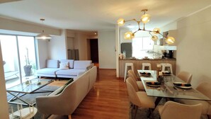 Ein modernes Wohnzimmer mit einer Couch, einem Glastisch und einer Küchenzeile mit Hockern.