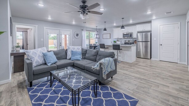 A modern living room with a gray sectional sofa, a glass coffee table, and a blue patterned rug.