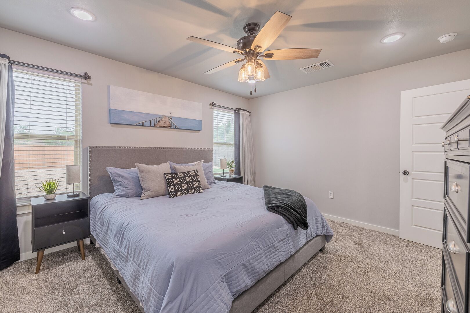 A bedroom with a bed, a ceiling fan, a nightstand, a dresser, and a window with blinds.