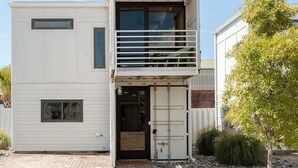 A modern two-story building with a balcony, a garage door, and a small tree in the yard. - Miller Loft at Container Park (Wilmington)