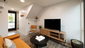A modern living room with a sofa, a coffee table, a TV on a wooden stand, and a chair. - Miller Loft at Container Park (Wilmington)