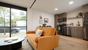 A modern kitchen with a sofa and coffee table, large windows, and a view of the street. - Miller Loft at Container Park (Wilmington)
