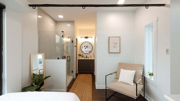 A modern hotel room with a bed, a sitting area with a chair, a small bathroom with a mirror, and a hallway leading to the bathroom. - Miller Loft at Container Park (Wilmington)