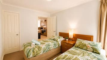 Habitación de hotel con dos camas, una mesita de noche, una lámpara y vista a la cocina.