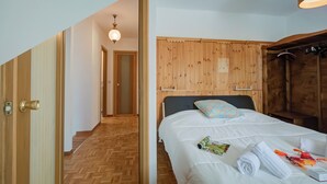 Ein Hotelzimmer mit Holz-Kopfteil, einem Bett mit weißer Bettwäsche, Holzboden und einem Flur, der zu einem anderen Zimmer führt.