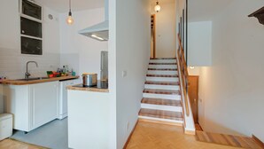 Eine Küche mit weißen Schränken, einer Holzarbeitsplatte und einem Spülbecken. Eine Holztreppe mit Treppenstufen und einer Leuchte darüber.