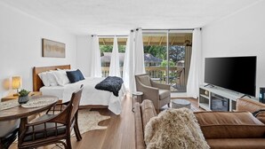 A modern hotel room with a bed, a sofa, a TV, and a balcony with a view of greenery.