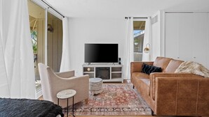 A living room with a flat-screen TV, a brown sofa, a small round table, and a patterned rug.