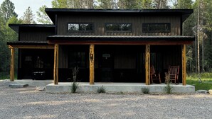 A modern two-story cabin with a covered porch, large windows, and a gravel driveway.