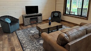 A living room with a fireplace, a television, a sofa, and a window with a view of a deck.