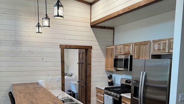 A modern kitchen with wooden cabinetry, a central island, stainless steel appliances, and pendant lighting.