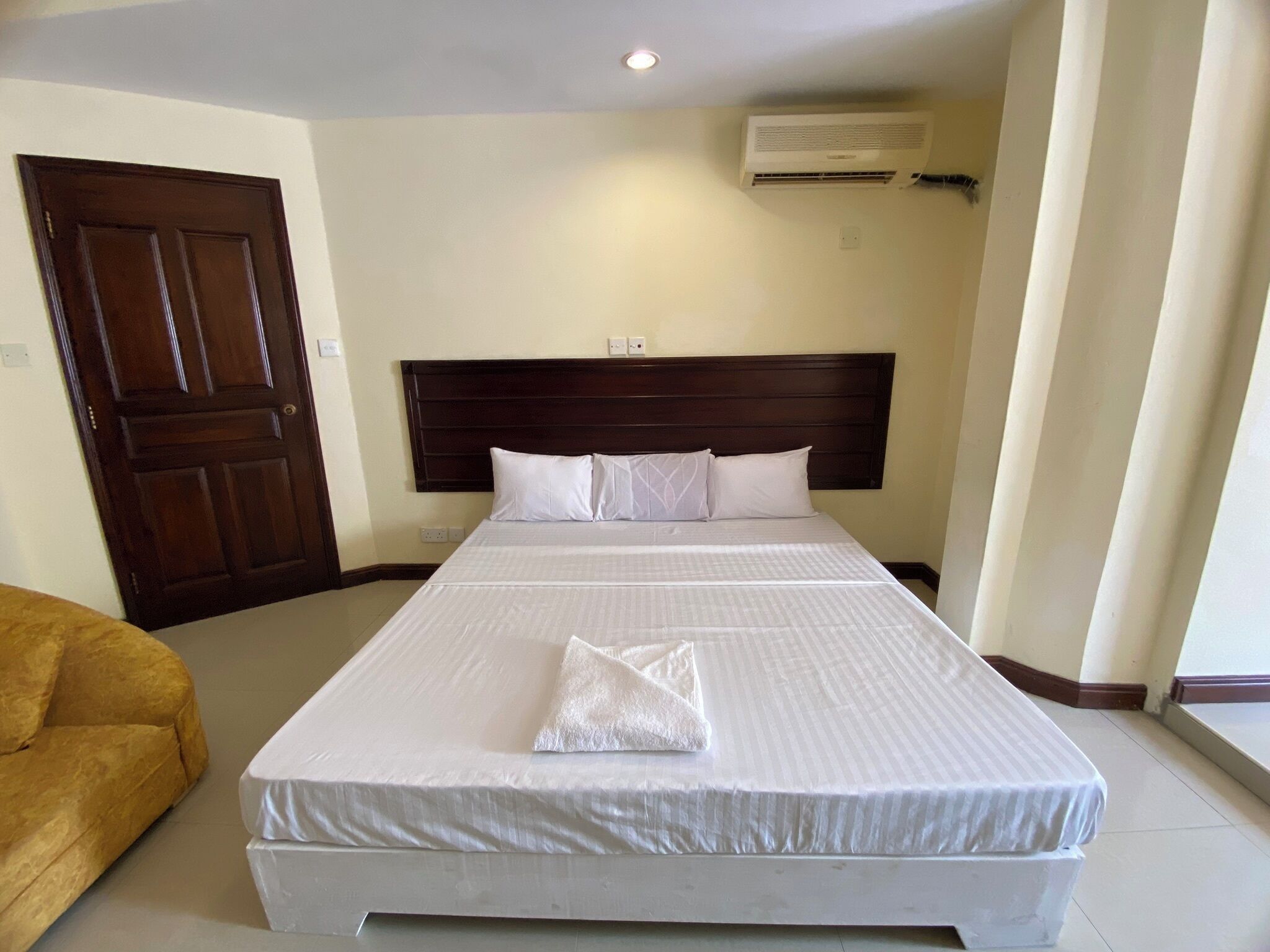 A hotel room with a large bed, a wooden headboard, a white mattress, and a brown door.