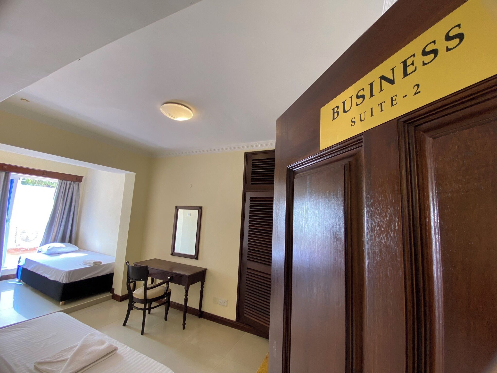 A hotel room with a bed, a desk, and a chair. There is a sign indicating it is 'Business Suite-2'.