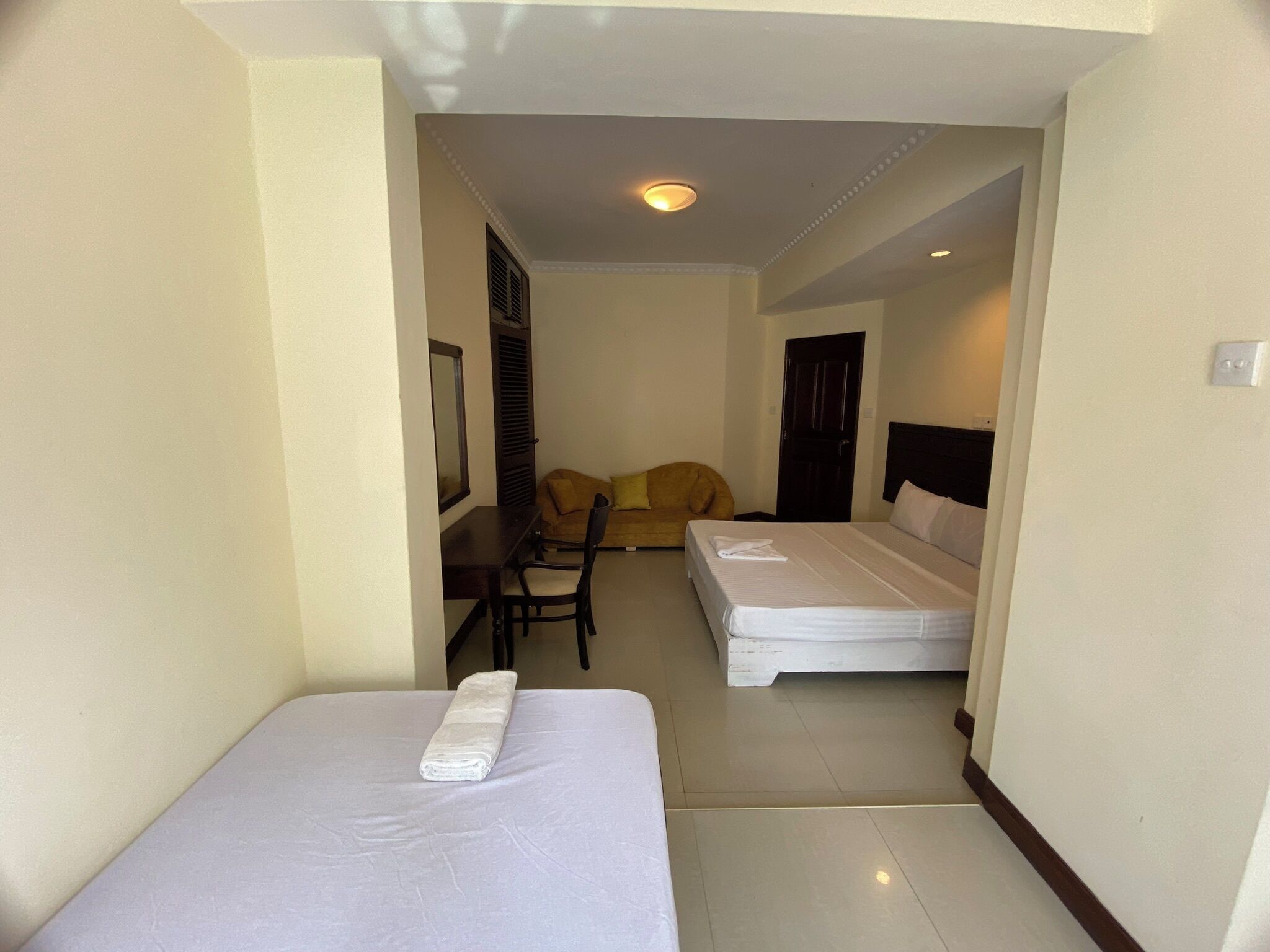 A hotel room with two single beds, a small desk, a chair, and a sofa.