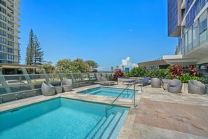 A rooftop pool area with two pools, lounge chairs, and a view of the cityscape. - Rhapsody Stunning Ocean Views Apartment (Surfers Paradise)