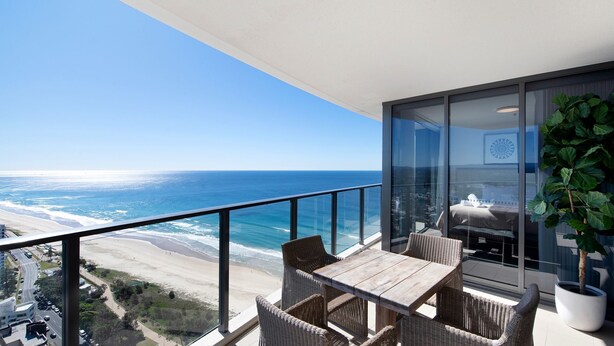 A balcony with a view of the beach and ocean, wicker furniture, and a potted plant. - Rhapsody Stunning Ocean Views Apartment - CoastHM (Surfers Paradise)