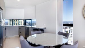 A modern kitchen with a dining area, large windows, and a city view. - Rhapsody Stunning Ocean Views Apartment - CoastHM (Surfers Paradise)