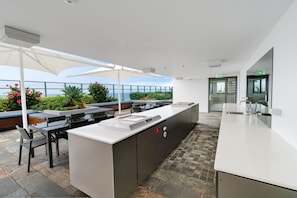 A modern outdoor kitchen area with a long counter, bar stools, and a seating area with a view of the sea. - Rhapsody Stunning Ocean Views Apartment (Surfers Paradise)