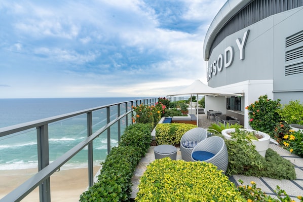 A seaside hotel with a balcony overlooking the ocean, featuring outdoor seating and lush landscaping. - Rhapsody Stunning Ocean Views Apartment (Surfers Paradise)