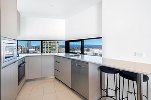 Une cuisine moderne avec vue sur la ville, équipée d’appareils électroménagers en acier inoxydable et dotée d’un coin bar avec des tabourets.