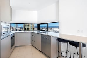 A modern kitchen with a city view, stainless steel appliances, and a bar area with stools. - Rhapsody Stunning Ocean Views Apartment (Surfers Paradise)