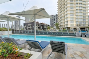 A pool area with lounge chairs and umbrellas, surrounded by high-rise buildings. - Rhapsody Stunning Ocean Views Apartment (Surfers Paradise)