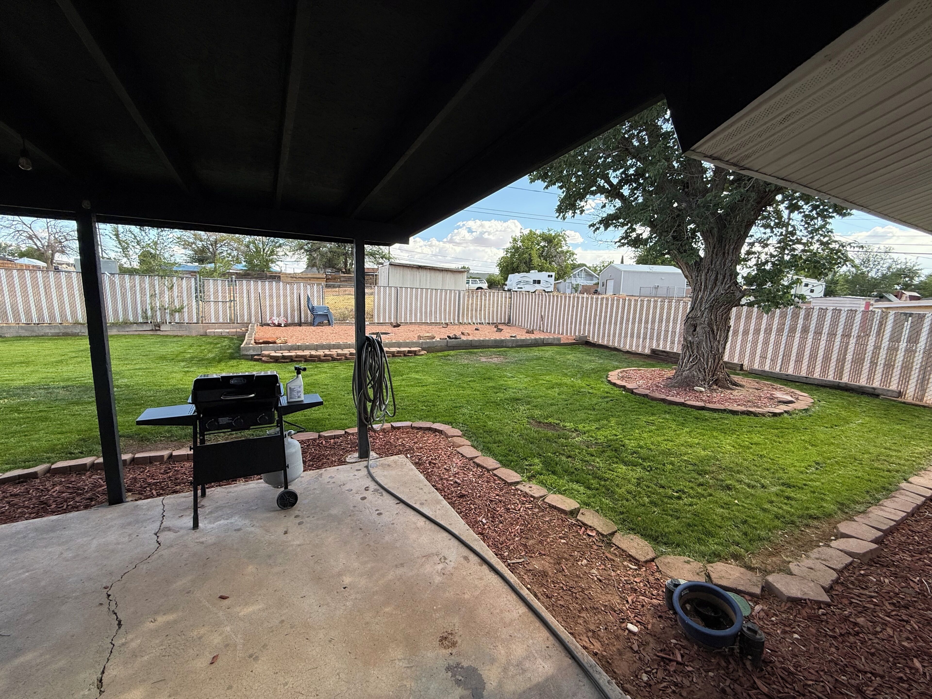 A covered patio area with a grill, a hose, and a tree.