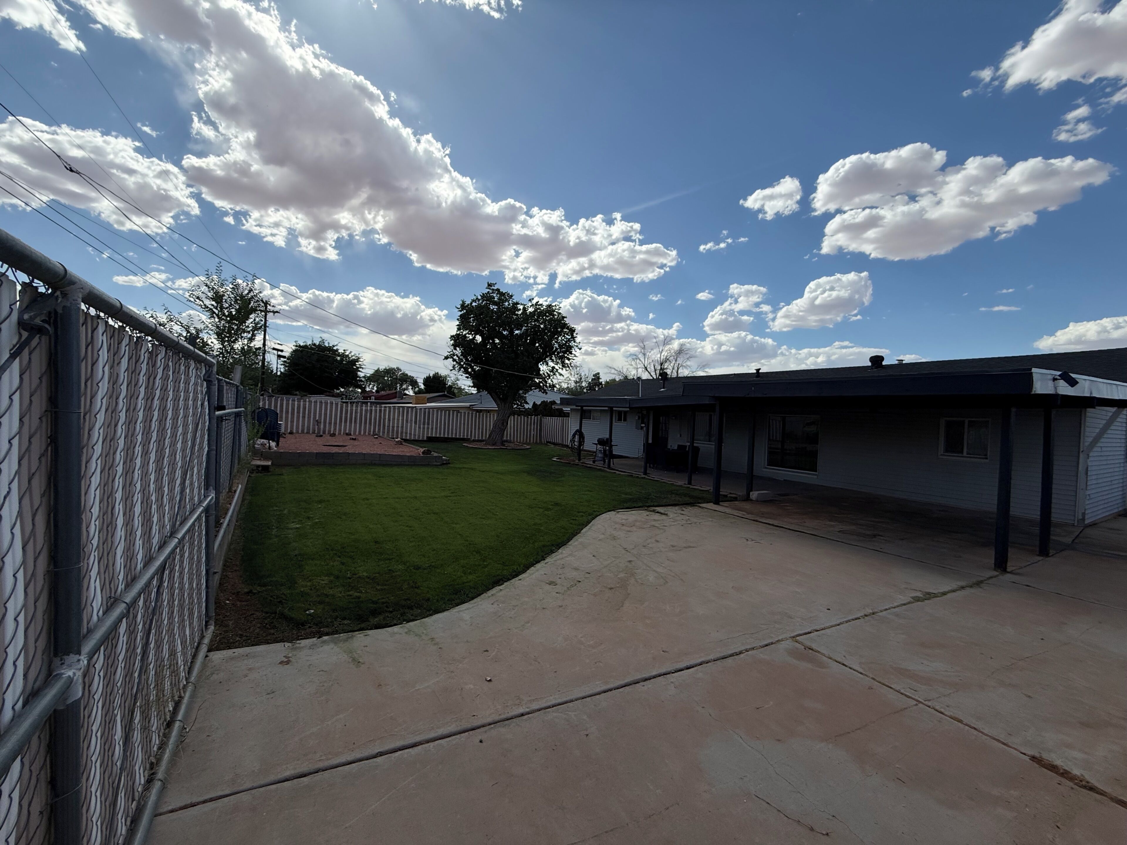 A fenced backyard with a grassy area, a concrete patio, and a building with a covered porch.