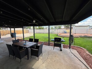 Un patio techado con mesa y sillas, una parrilla y vista al jardín trasero.