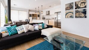 Una sala de estar moderna con un sof á negro, una mesa de centro de vidrio y una cocina al fondo.