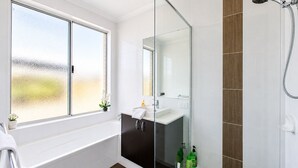Un baño moderno con cabina de ducha de vidrio, bañera y ventana con vidrio esmerilado.