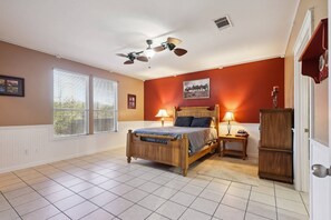 A bedroom with a bed, two bedside tables, a ceiling fan, a window with blinds, and a door.