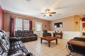 A living room with a leather sofa, a wooden coffee table, a TV mounted on the wall, and a ceiling fan.