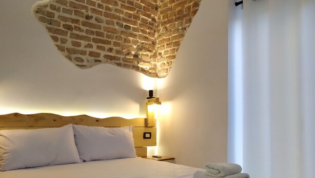 A hotel room with a brick-patterned ceiling, a wooden headboard, a bedside lamp, and neatly folded towels on the bed. - A-1 · Cosy Modern Studio With Balcony in Blloku (Tiranë)