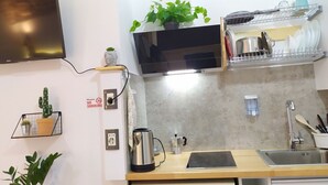 A modern kitchen with a flat-screen TV mounted on the wall, a coffee maker, and a dish rack. - A-1 · Cosy Modern Studio With Balcony in Blloku (Tiranë)
