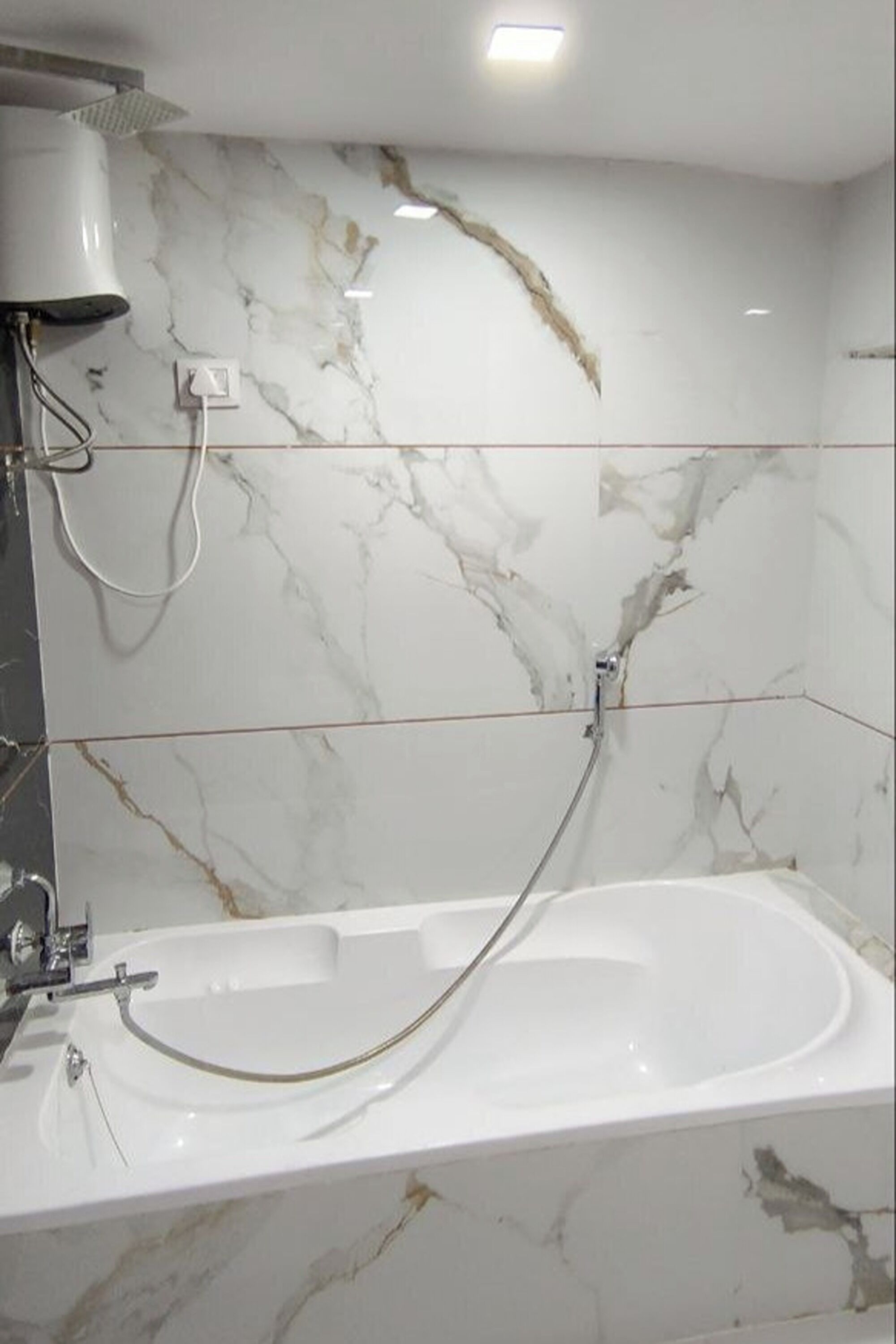 Baño con bañera blanca, paredes de mármol y ducha de mano.