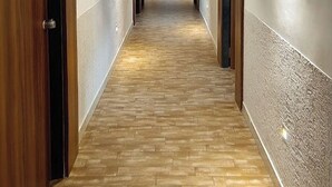 Ein langer, schmaler Korridor mit Holztüren an einer Seite und einer strukturierten Wand an der anderen.