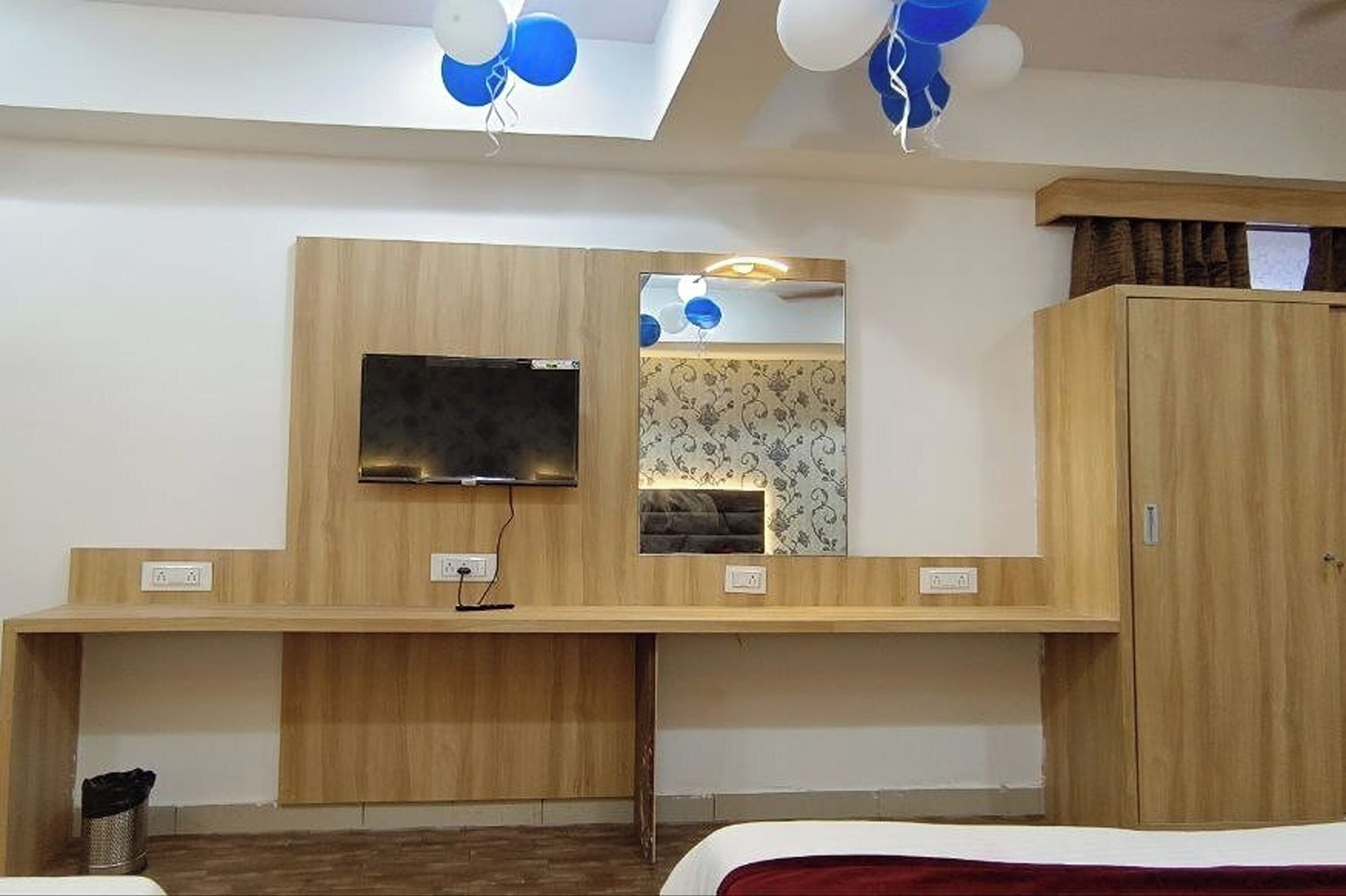 A hotel room with a wooden desk, a flat-screen TV, a wardrobe, and a mirror.