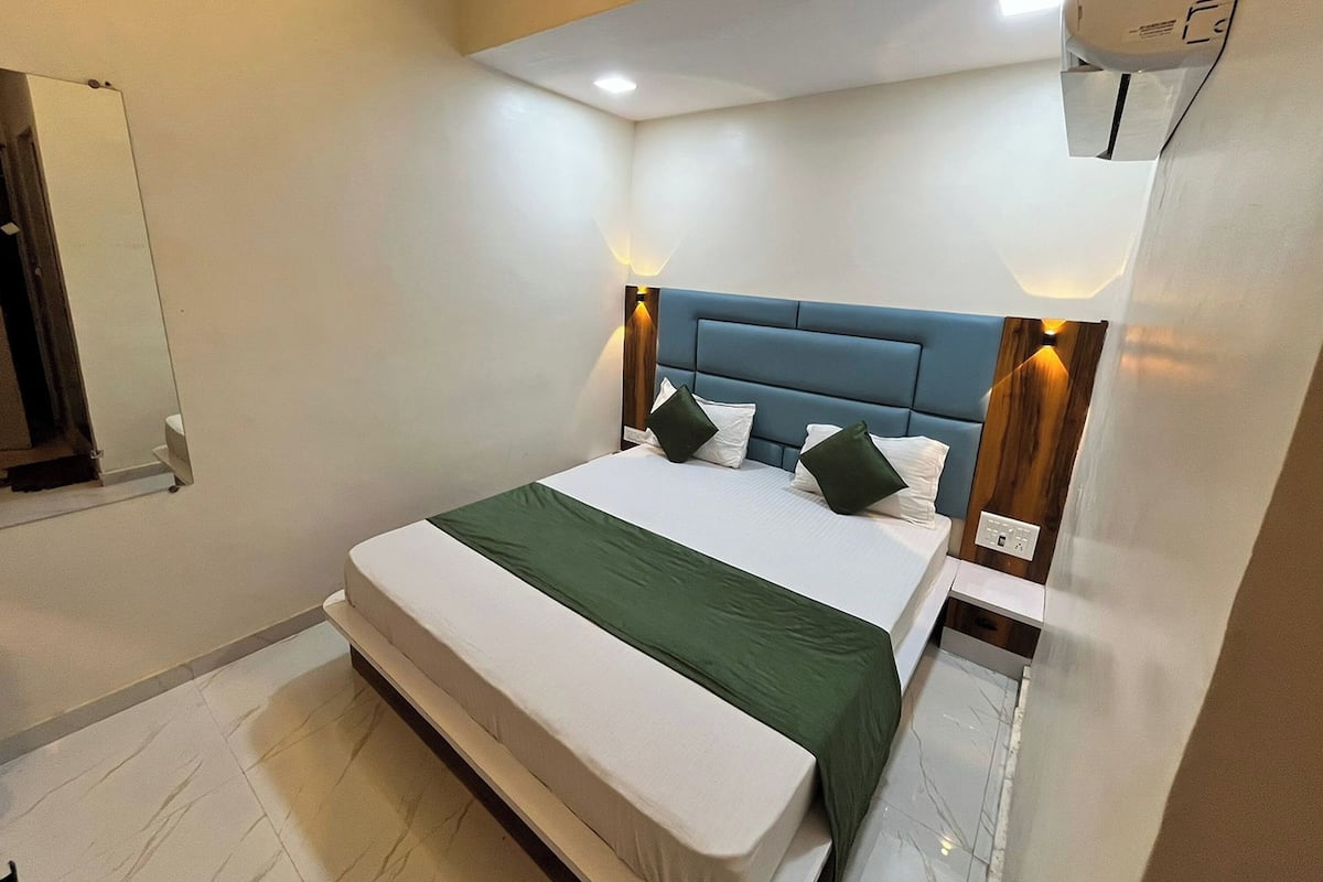 A modern hotel room with a large bed, a blue headboard, and a wall-mounted air conditioning unit.