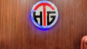 En rund skylt med bokstäverna ”HG” på en vägg av trä.
