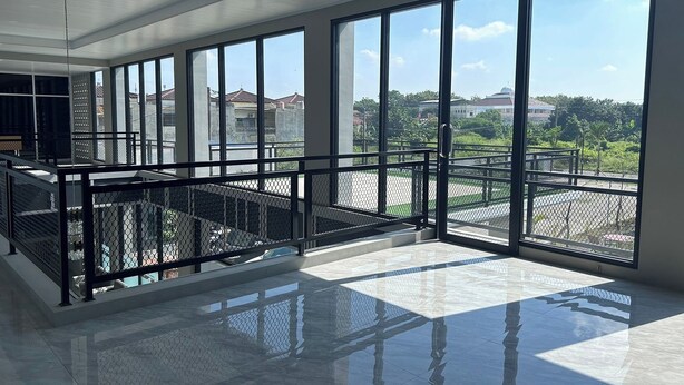 A spacious balcony with large windows overlooking a parking area and greenery. - Gs 2 Syariah (Surakarta)