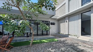 A modern outdoor patio area with a seating arrangement, a small tree, and a gravel pathway. - Gs 2 Syariah (Surakarta)