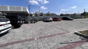 A parking area with several cars and motorcycles, a building with a concrete facade, and a clear blue sky. - Gs 2 Syariah (Surakarta)