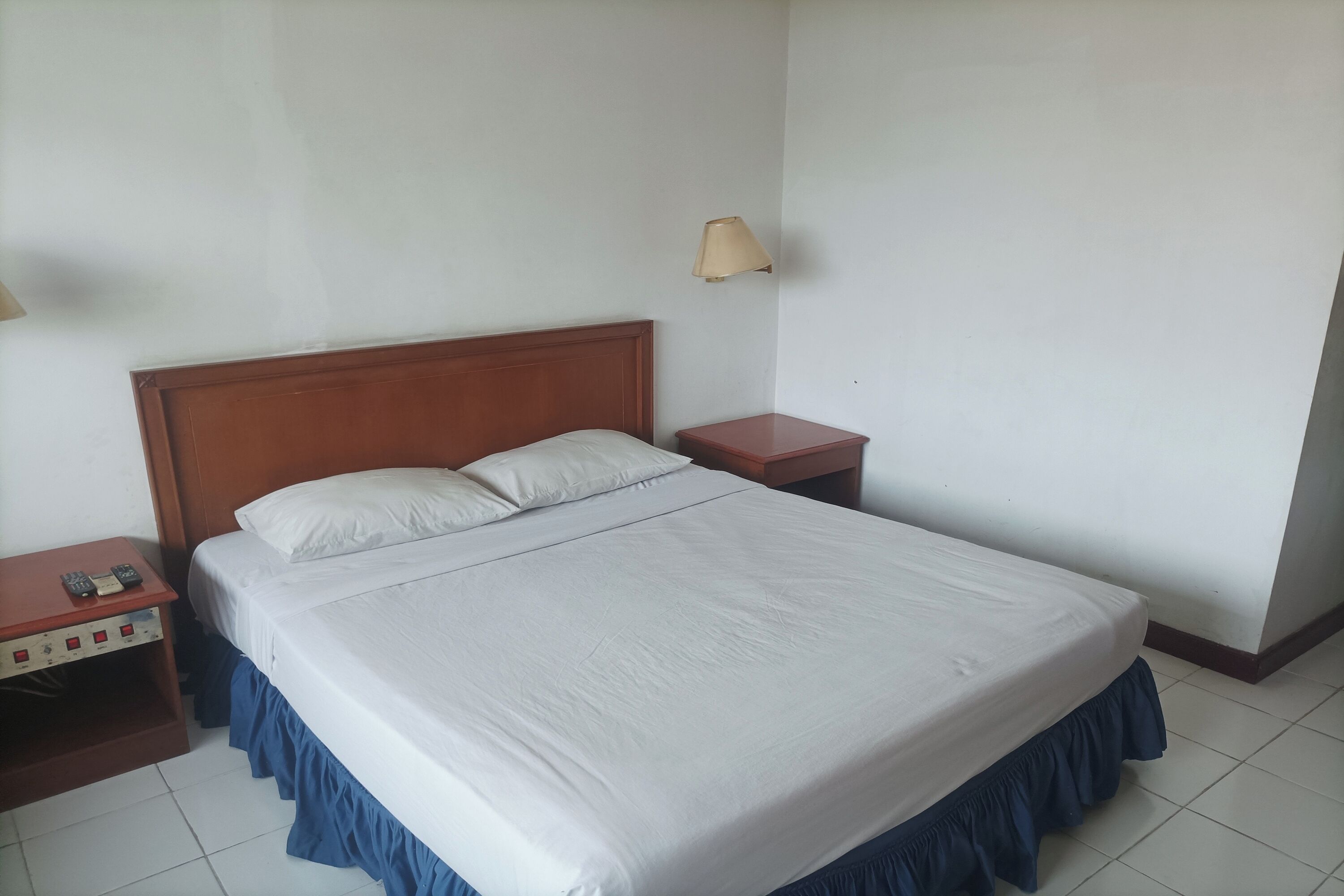 A neatly made bed with a wooden headboard, a bedside table with a lamp, and a power strip.