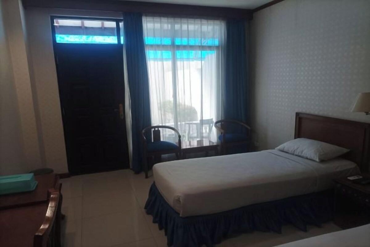 A hotel room with a bed, a desk, two chairs, a window with curtains, and a door.