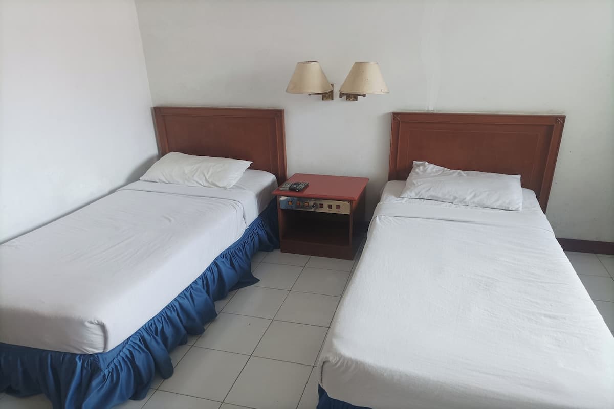 Une chambre d’hôtel avec deux lits simples, une table de chevet avec une télécommande et deux lampes fixées au mur.